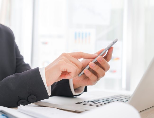 Closeup of business woman hand typing on laptop keyboard with  mobile phone